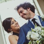 A bride and groom smiling in front of a window.