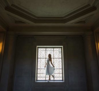 A woman in a white dress standing in front of a window.